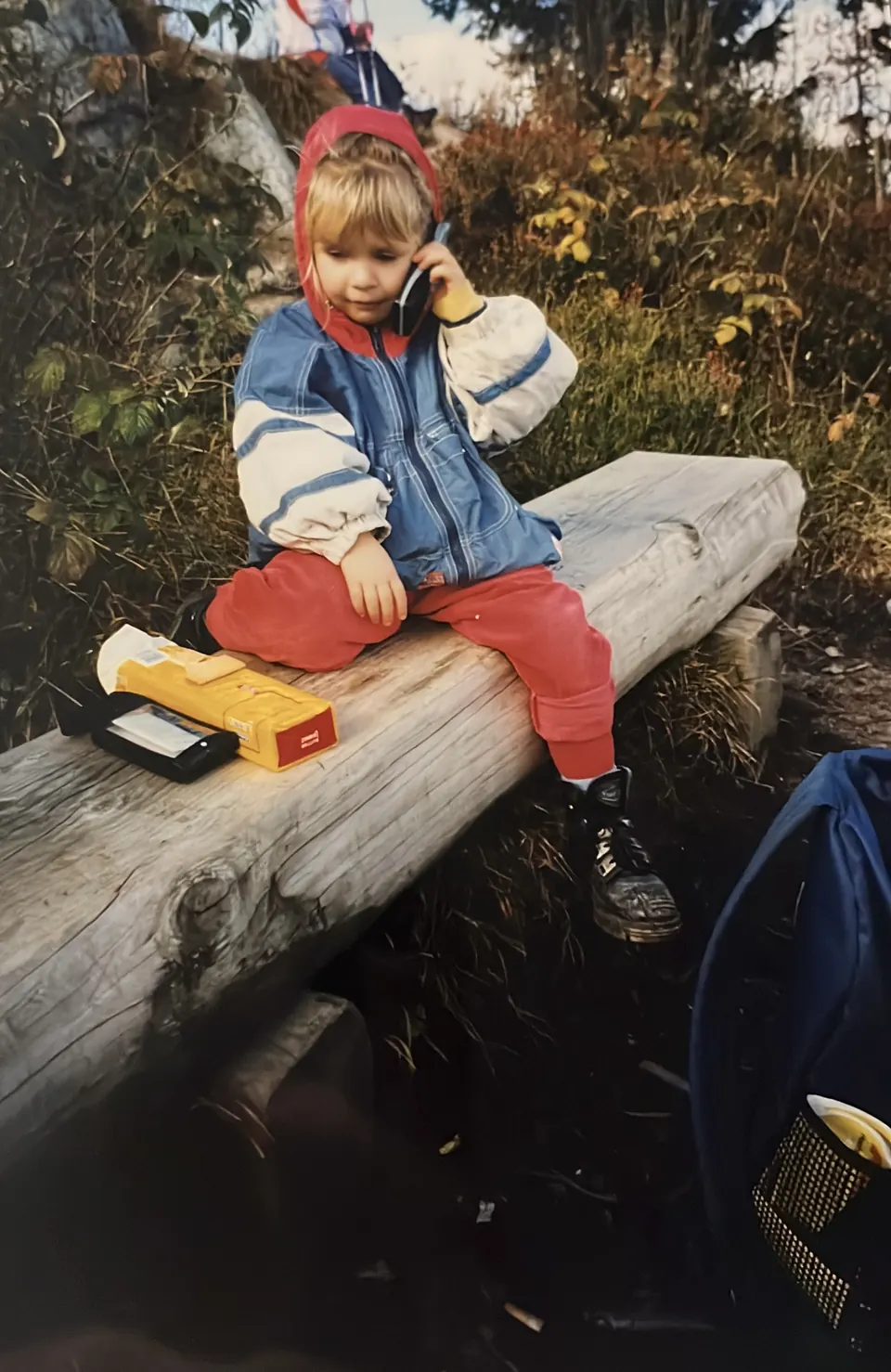 Marlen Weber als Kind mit Spielzeugtelefon auf einem Baumstamm